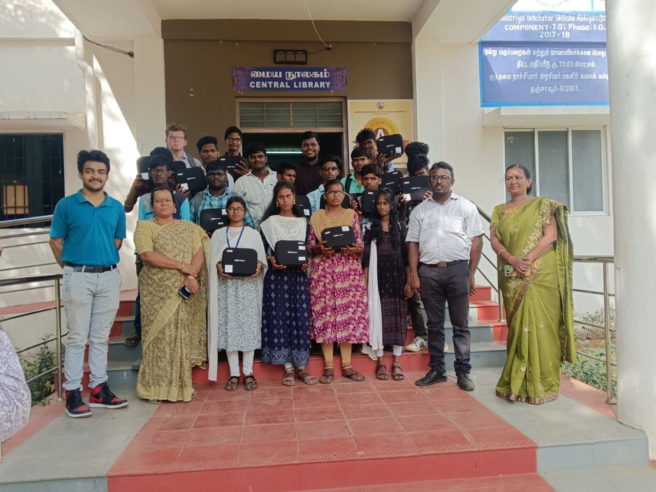 Group photo of visually impaired students holding Aura Vision glasses with HTBF staff during the distribution at Kundavai Nachiyar Government Arts College for Women.