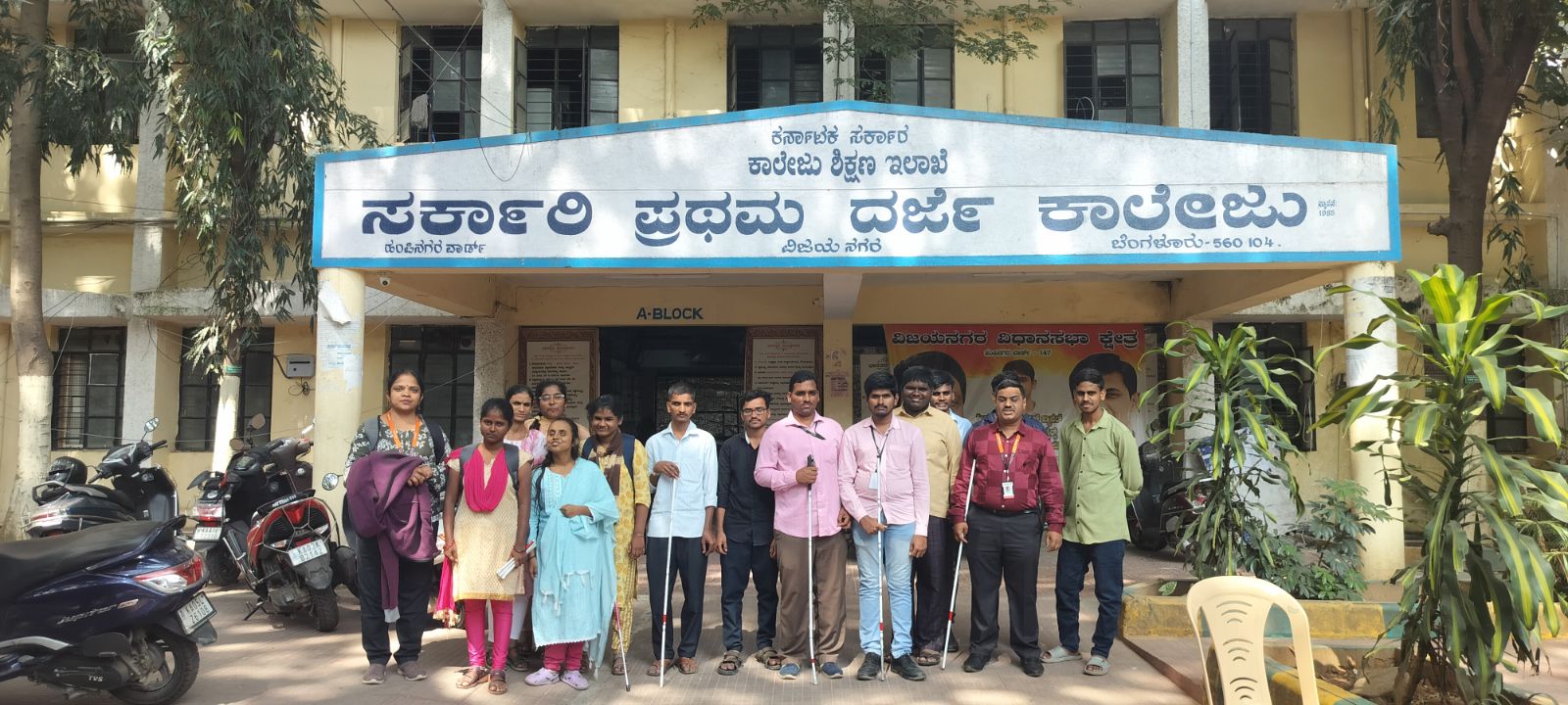 A group photo of visually impaired EMET students standing outdoors along with HTBF trainer Ms. Valarmathy Senthilkumar at Government First Grade College, Vijayanagara.