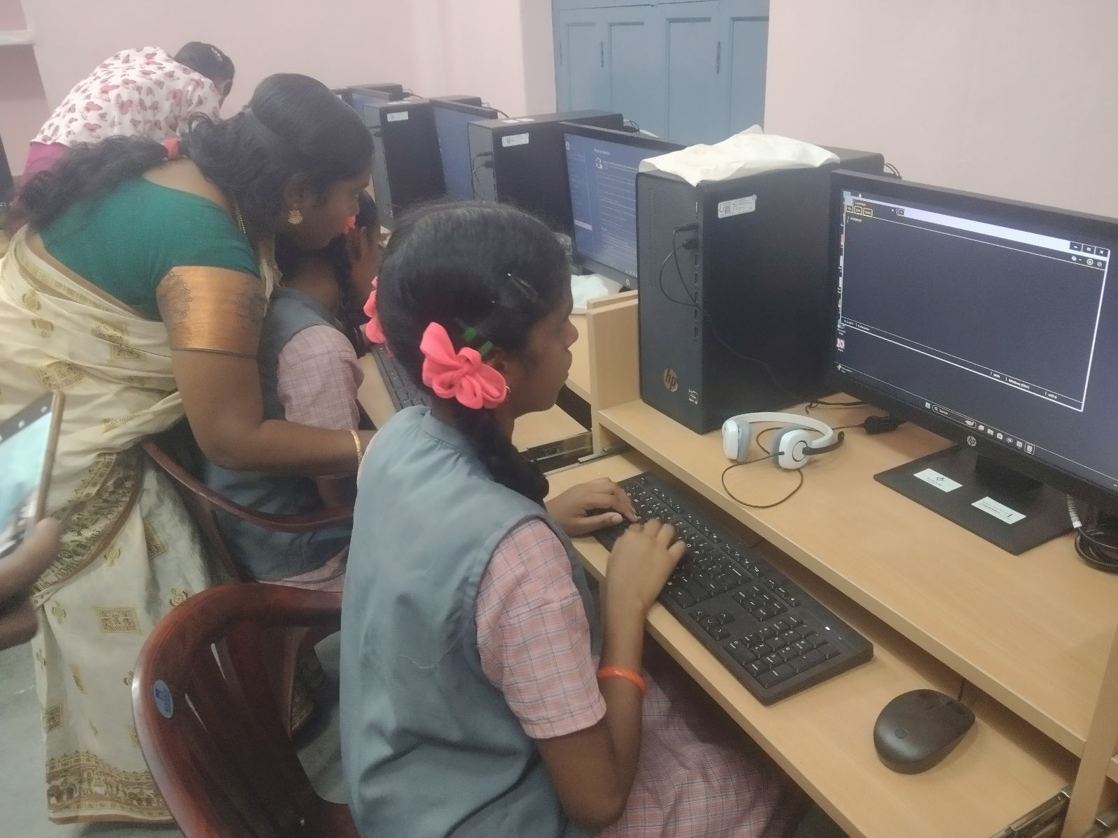 Visually impaired students work on computers at the Government Higher Secondary School for the Visually Impaired in Thanjavur, as a teacher stands beside them providing guidance.