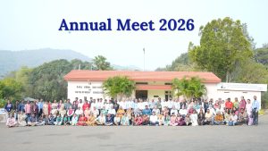 A group photo of HTBF trustees, staff, trainers, volunteers, entrepreneurs, and community members gathered outside the Karl Kübel Institute for Development Education building. The entire group is arranged in rows in front of the campus building with palm trees on either side, rolling hills in the background, and the title “Annual Meet 2026” displayed at the top of the image.